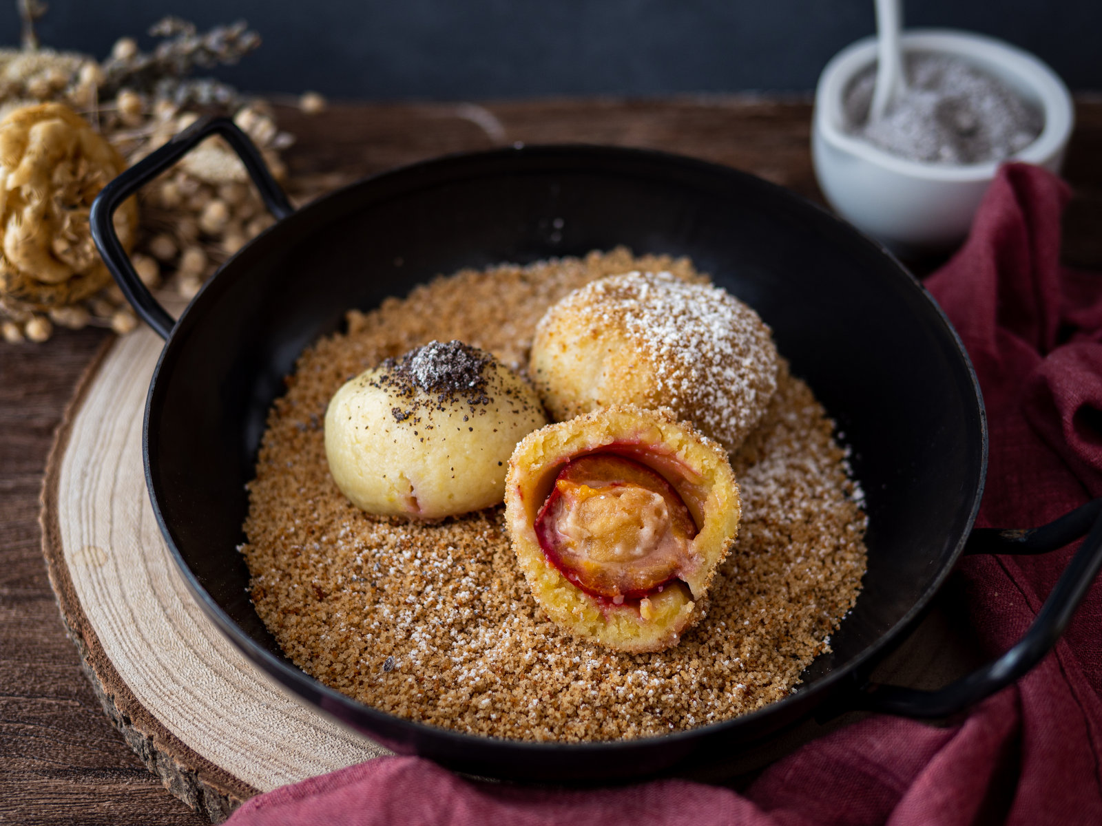 Zwetschgenknödel mit Marzipan, in Paniermehl gewälzt und mit Puderzucker bestreut, auf einem Teller angerichtet.