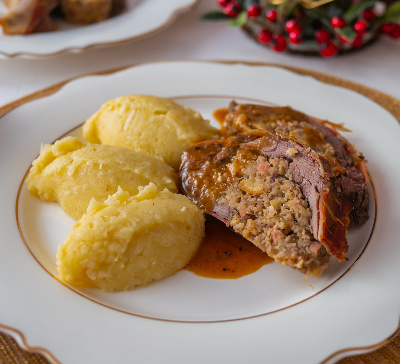 Rehrückenroulade in Scheiben geschnitten mit Kastanienfüllung und Sellerie-Kartoffel-Püree auf einem Teller angerichtet.