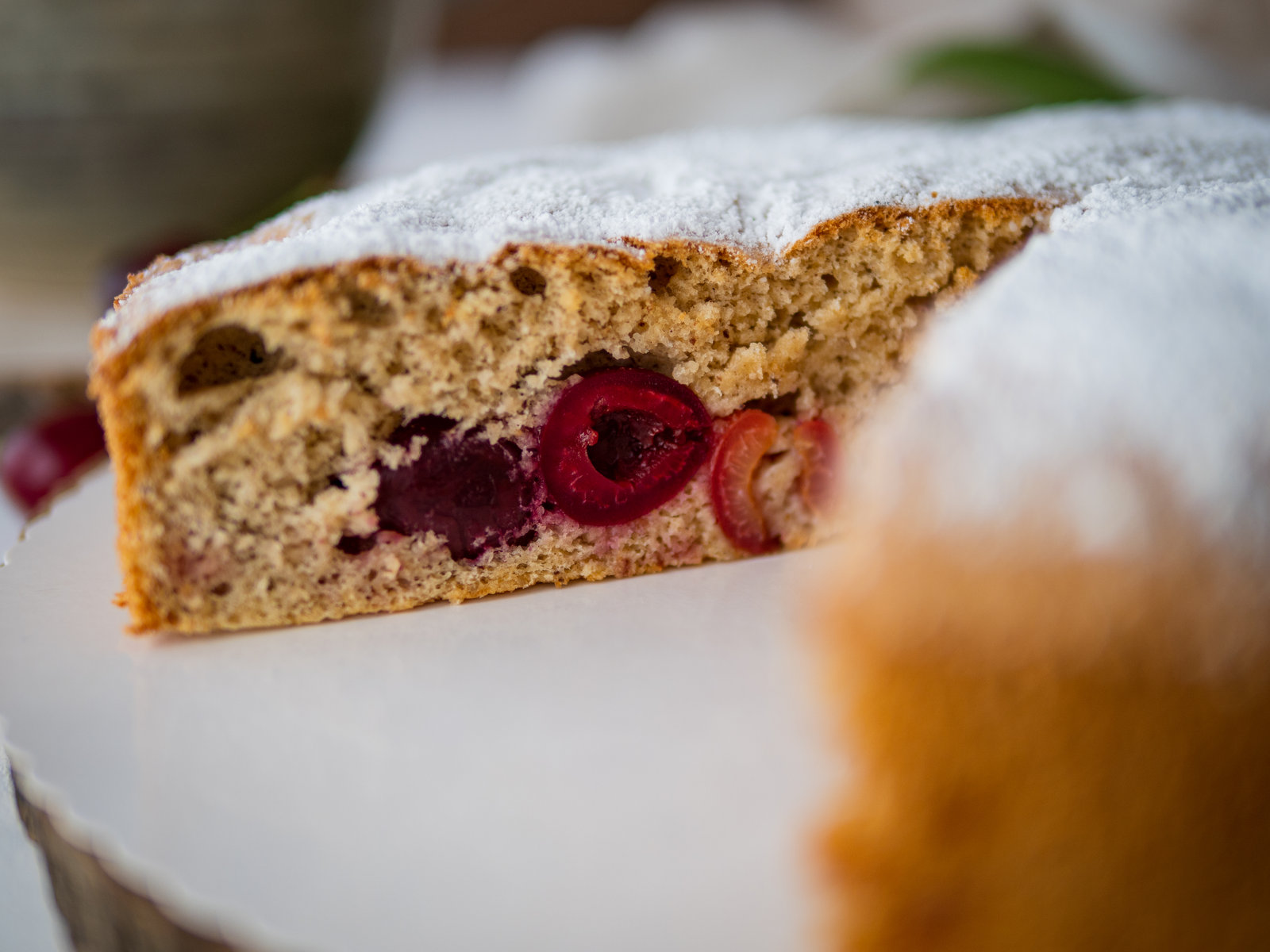Ein Stück Süßkirschkuchen mit Puderzucker bestreut auf einem Teller, daneben frische Kirschen.