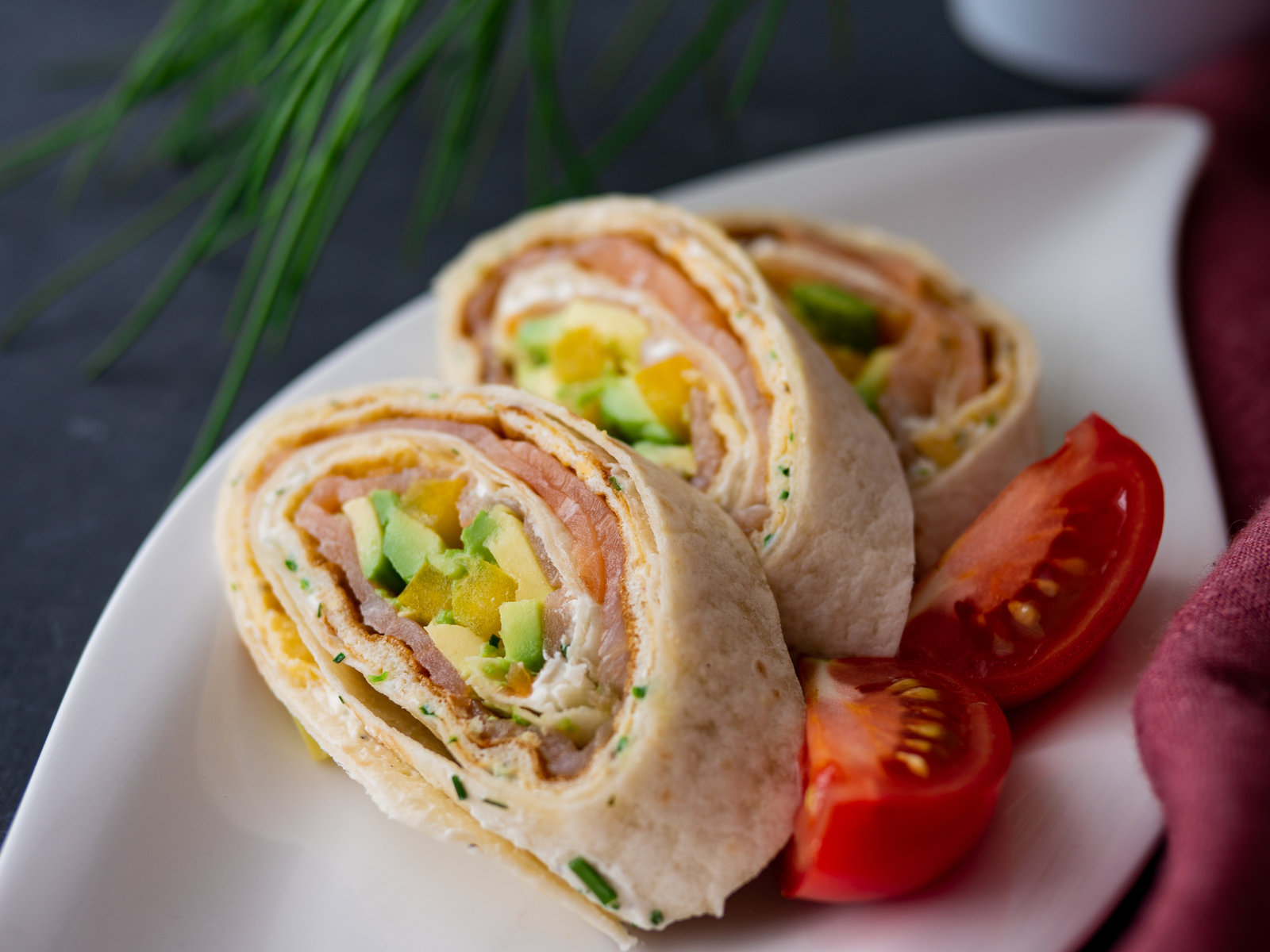 Aufgeschnittene Lachsröllchen mit Avocado, Paprika und Ei auf einem Teller angerichtet.