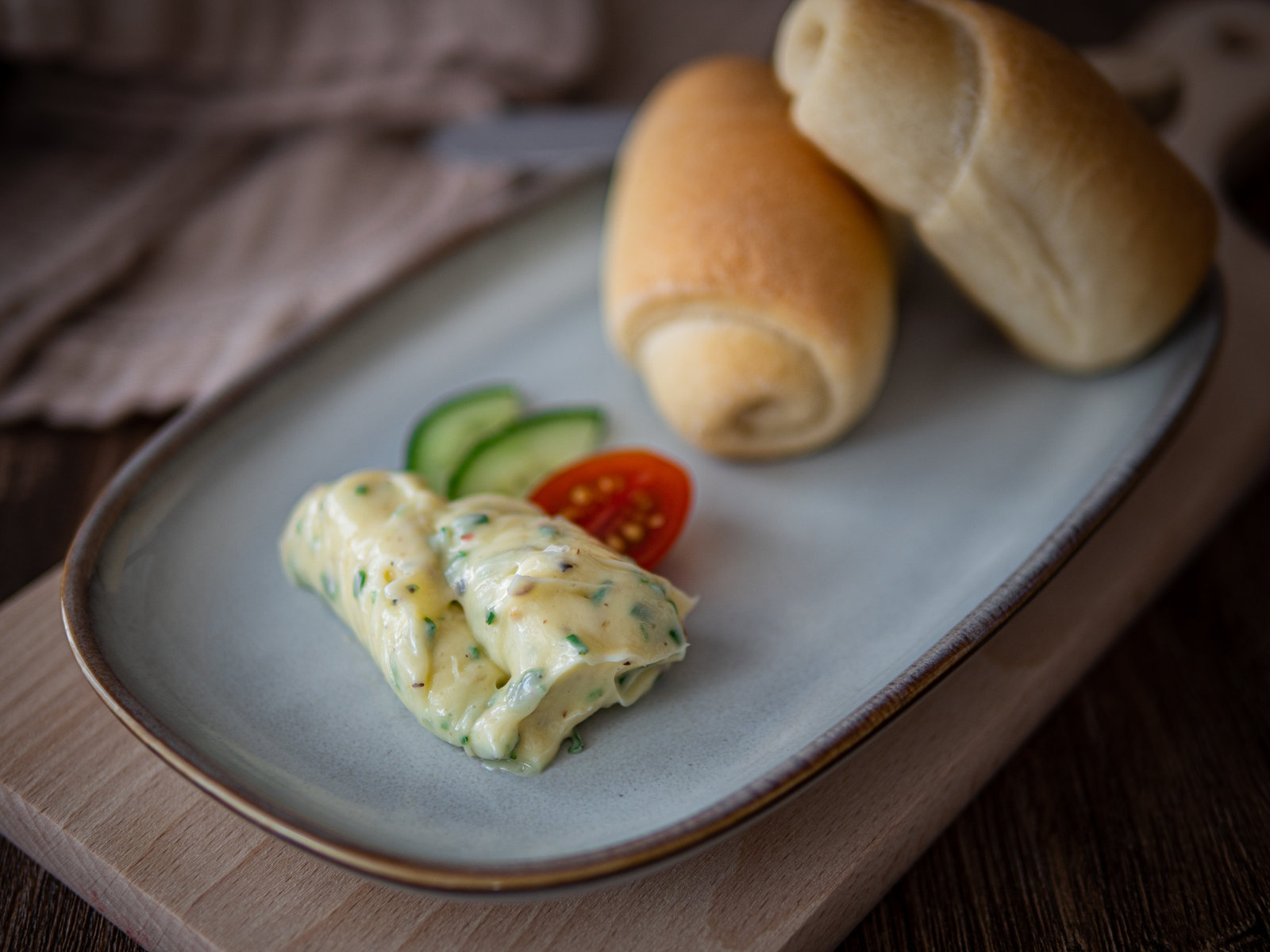 Eine Schale mit Schnittlauch-Butter, daneben kleine Brötchen, Minitomaten und Gurkenscheiben.