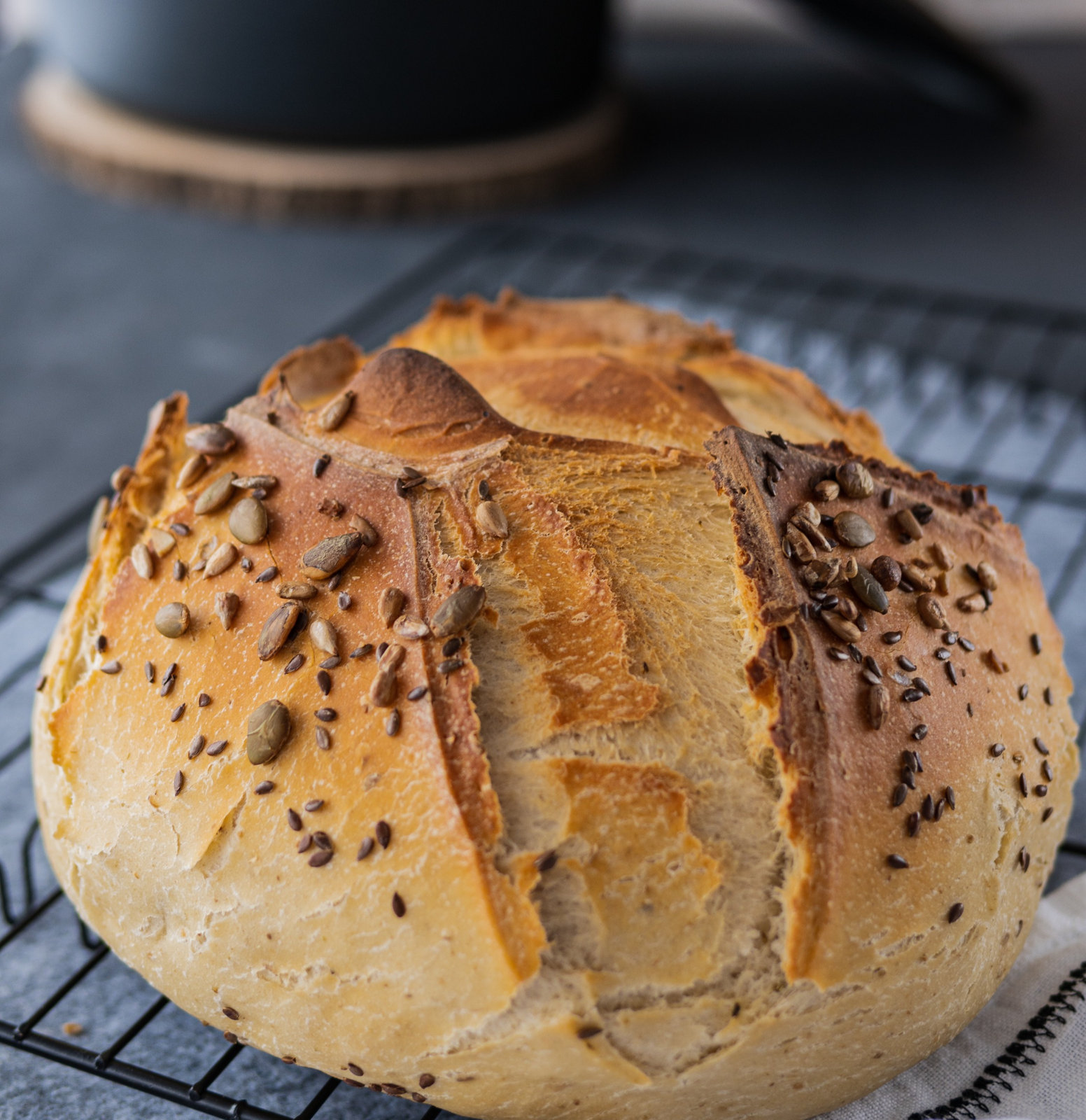 Ein frisch gebackenes, rundes Dinkelbrot mit Joghurt, bestreut mit Kernen, auf einem Holzbrett.