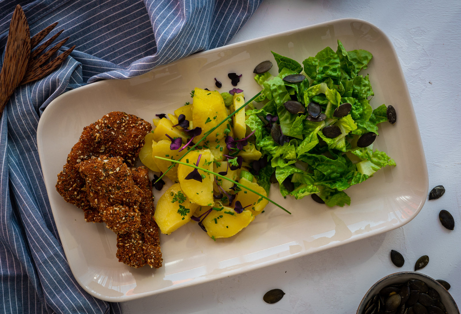 Backhendl-Salat mit Kürbispanade und Kartoffelsalat auf einem Teller angerichtet
