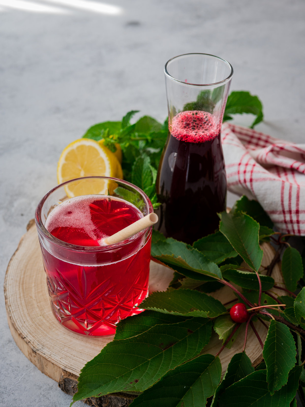 Drei Flaschen selbstgemachter Kirschsirup mit Erdbeeren und Minze, daneben frische Kirschen, Erdbeeren und Minzblätter.