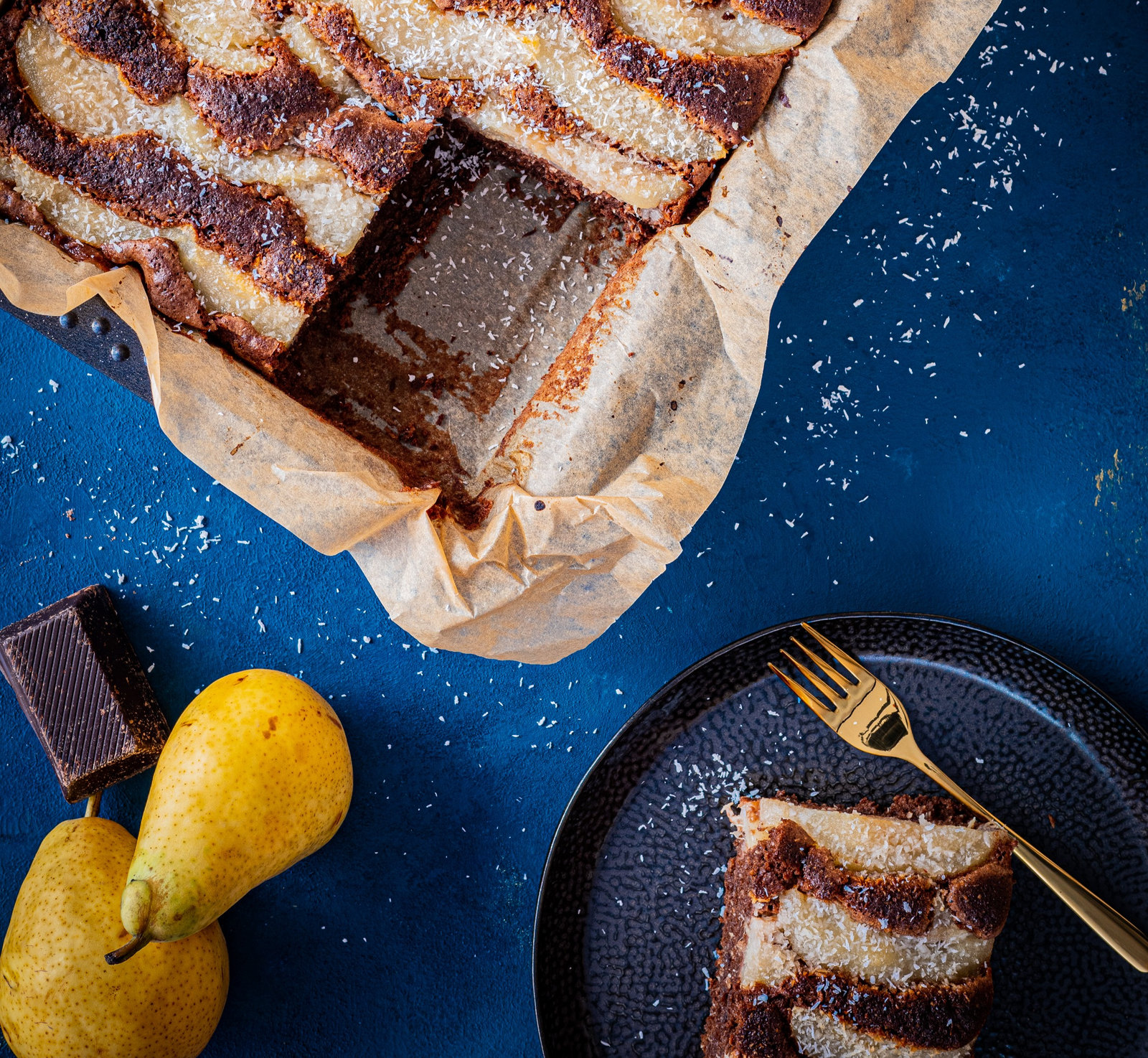 Ein Stück Schoko-Kokos-Birnen-Kuchen mit Puderzucker bestreut auf einem Teller