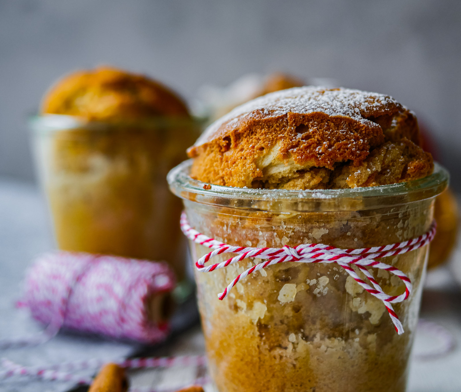 Vier Gläser mit gebackenem Apfelkuchen, bestreut mit Puderzucker.