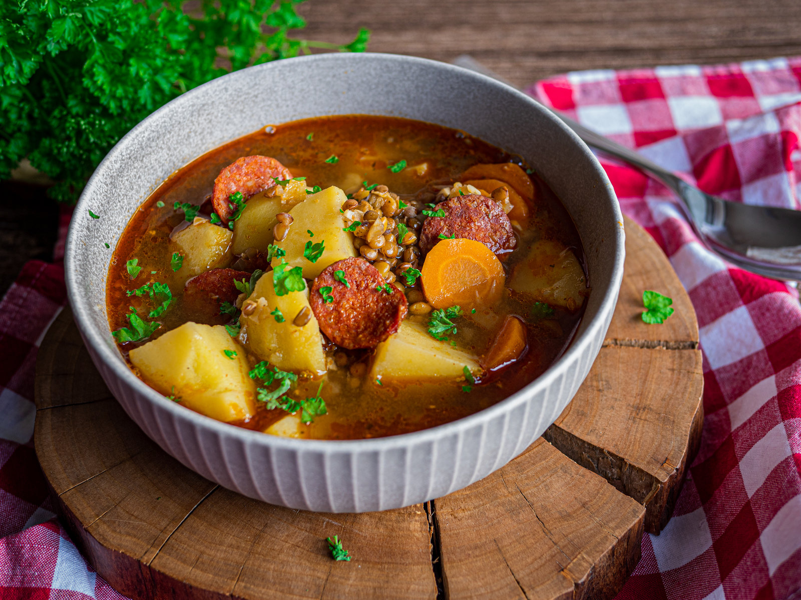 Eine Schale ungarische Linsensuppe mit Kolbász, Kartoffeln und Karotten, garniert mit frischen Kräutern.