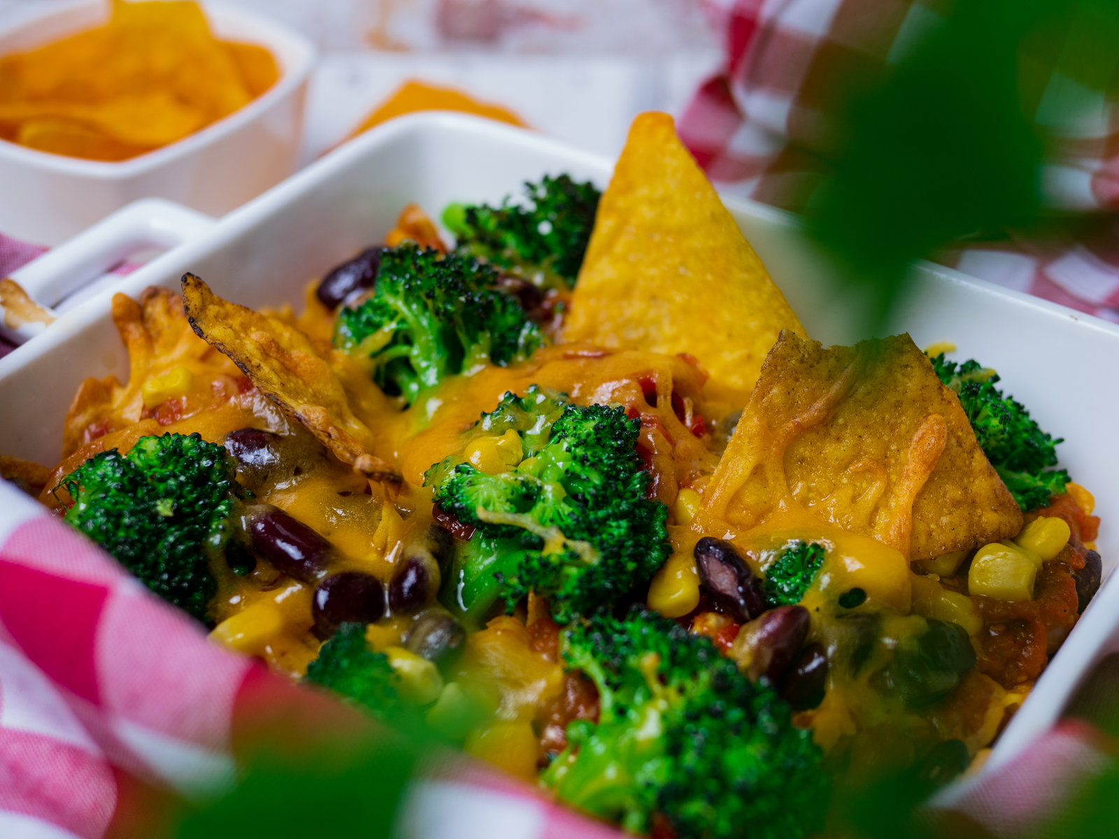 Nahaufnahme von überbackenen Nachos mit geschmolzenem Käse, Salsasauce, Brokkoli, Mais und Kidneybohnen in einer Auflaufform.