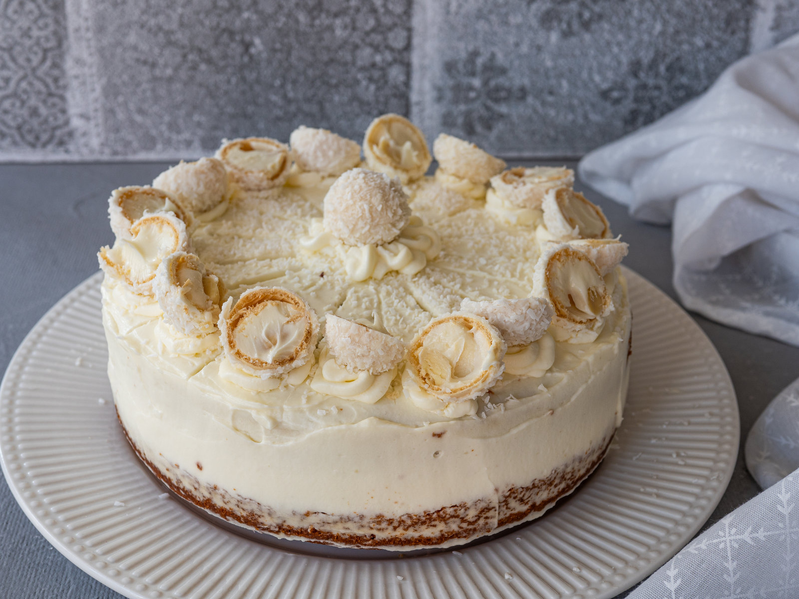 Eine angeschnittene Raffaello-Torte mit Kokosraspeln und Raffaellos dekoriert