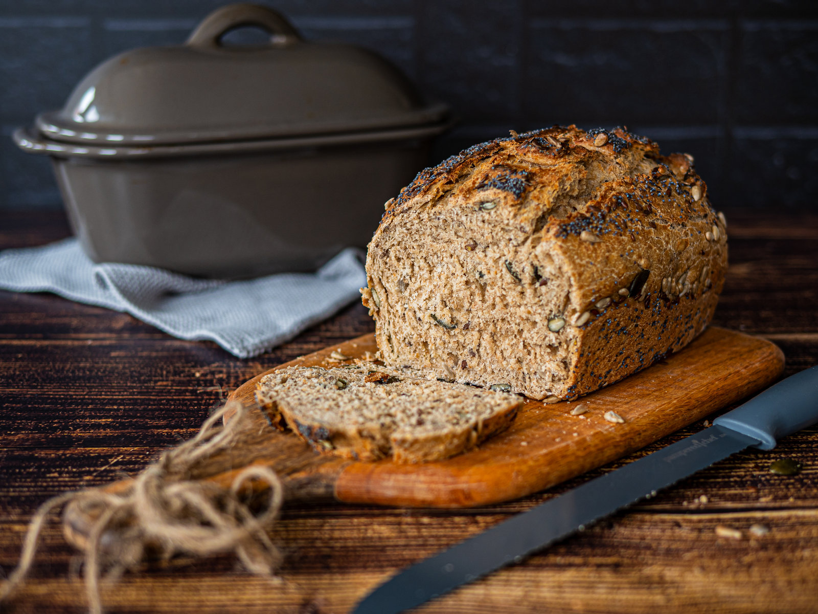 Ein frisch gebackenes, angeschnittenes Körnerbrot mit knuspriger Kruste und sichtbaren Körnern, das auf einem Holzbrett liegt.