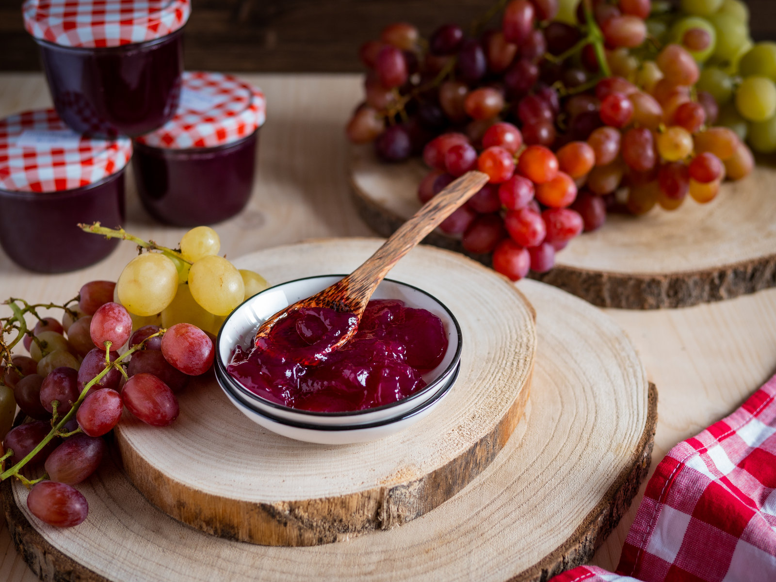 Mehrere Gläser mit selbstgemachtem, violettem Traubengelee, teilweise mit Etiketten versehen, auf einem Holztisch.
