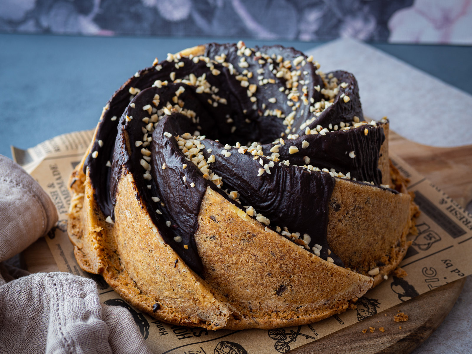 Ein angeschnittener Apfelgugelhupf, bestäubt mit Puderzucker, auf einer Kuchenplatte.