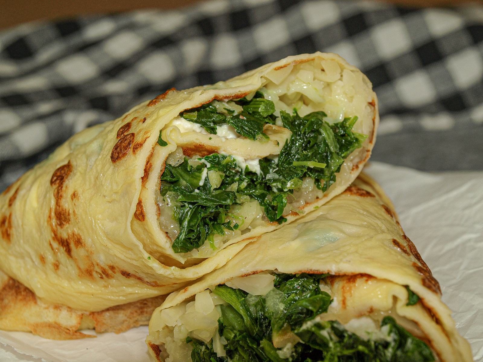 Gerollte Palatschinken mit Spinat-Frischkäse-Füllung, mit Käse bestreut