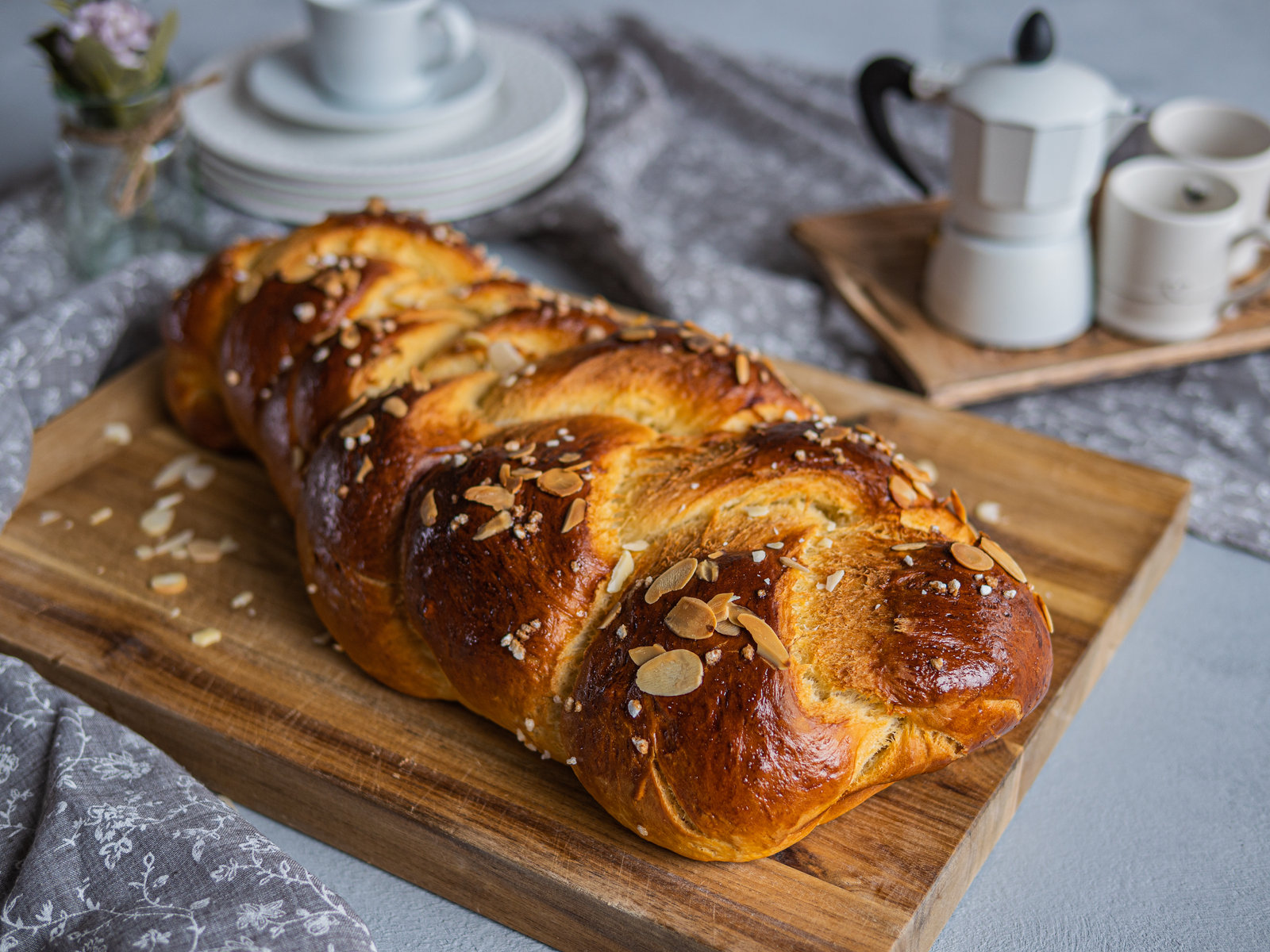 Ein goldbraun gebackener Dinkelzopf, bestreut mit Mandelblättchen und Hagelzucker, auf einem Backblech.
