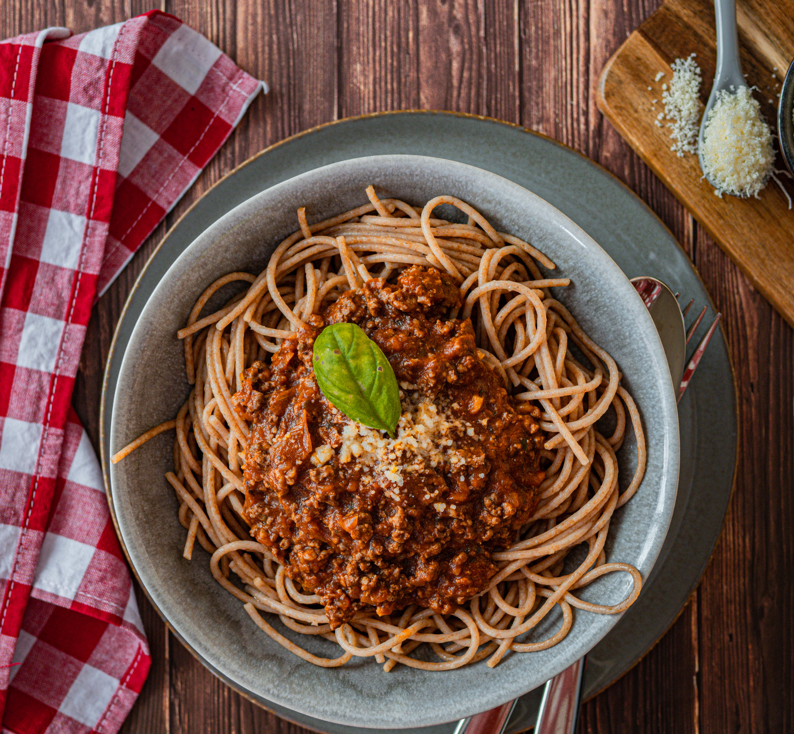 Teller mit Rehbolognese und Nudeln, bestreut mit Parmesan und frischen Kräutern