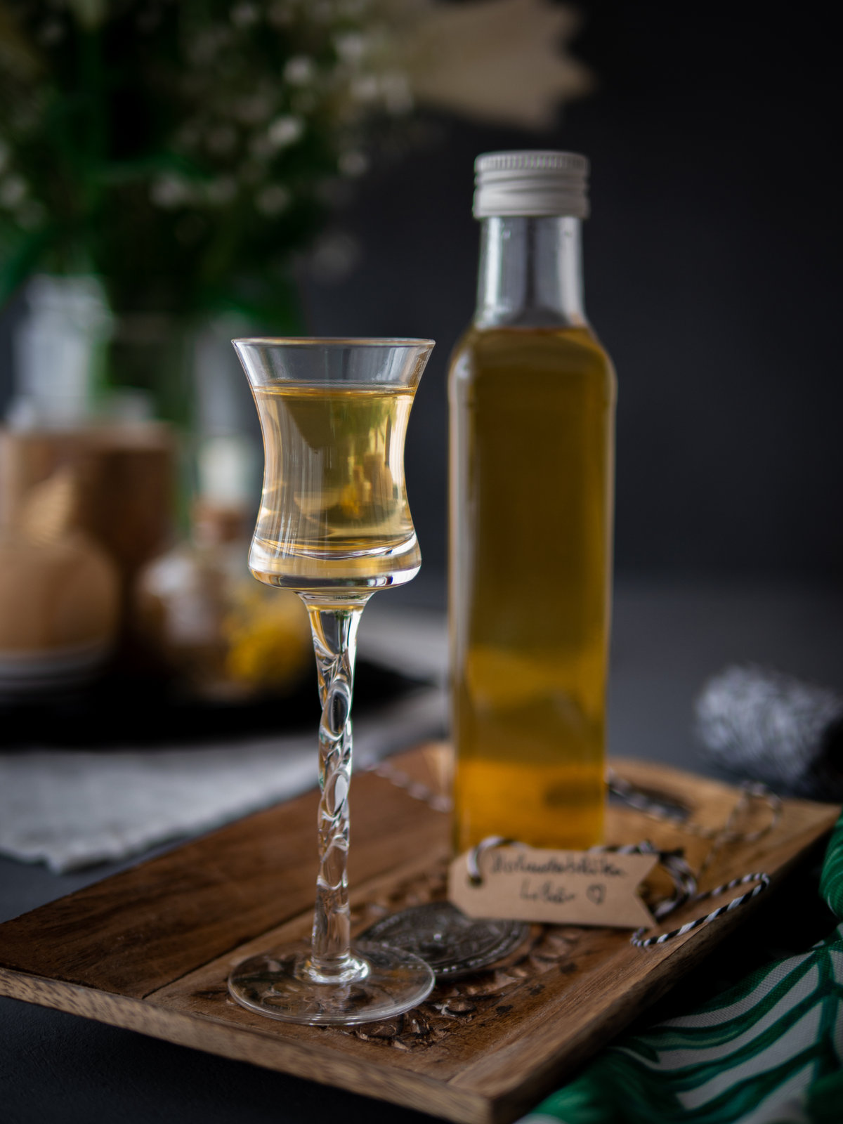 Selbstgemachter Holunderblütenlikör in einer Flasche mit Holunderblüten im Hintergrund.