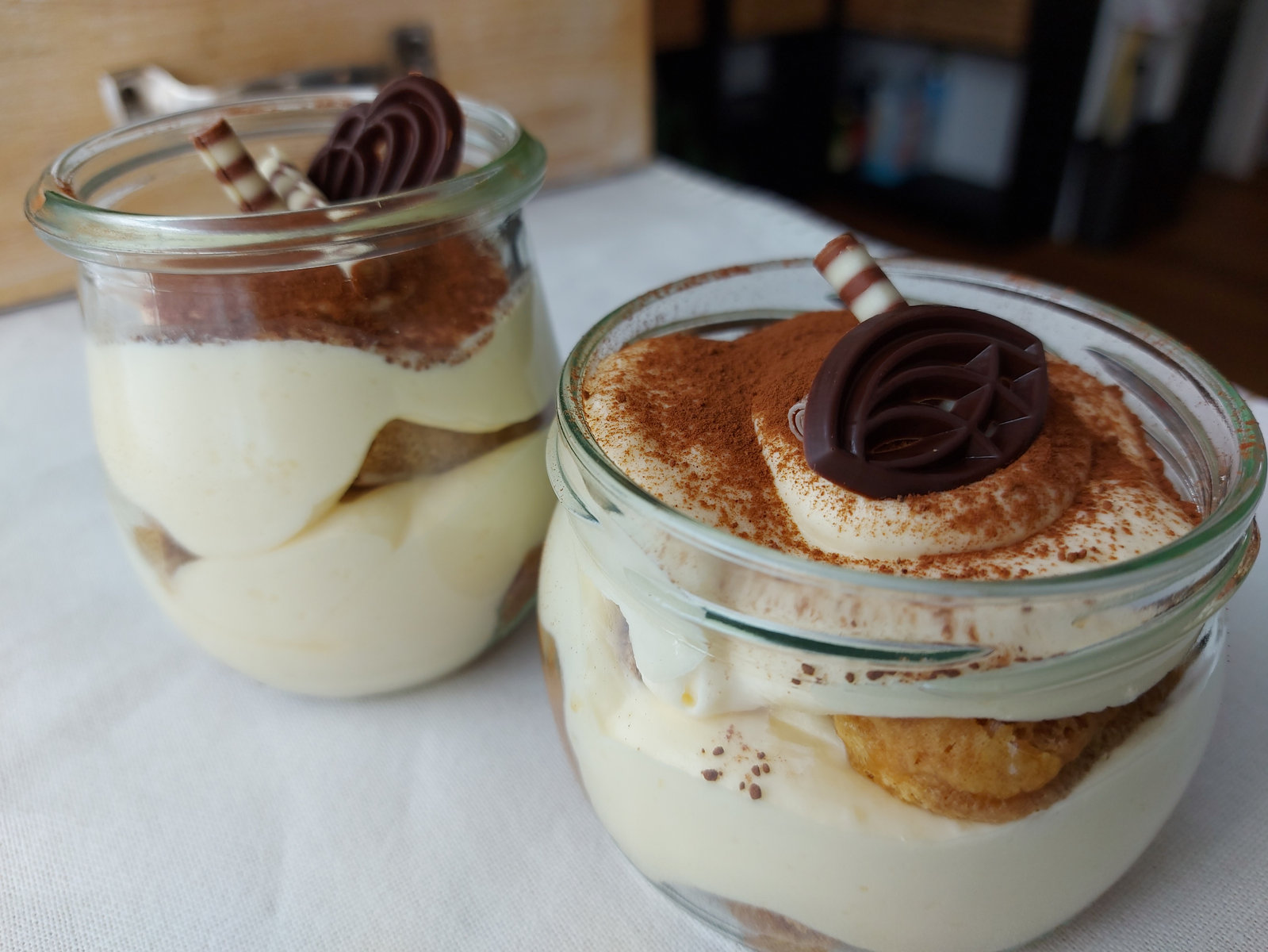 Tiramisu im Glas, geschichtet mit Löffelbiskuits und Mascarponecreme, bestreut mit Kakaopulver.