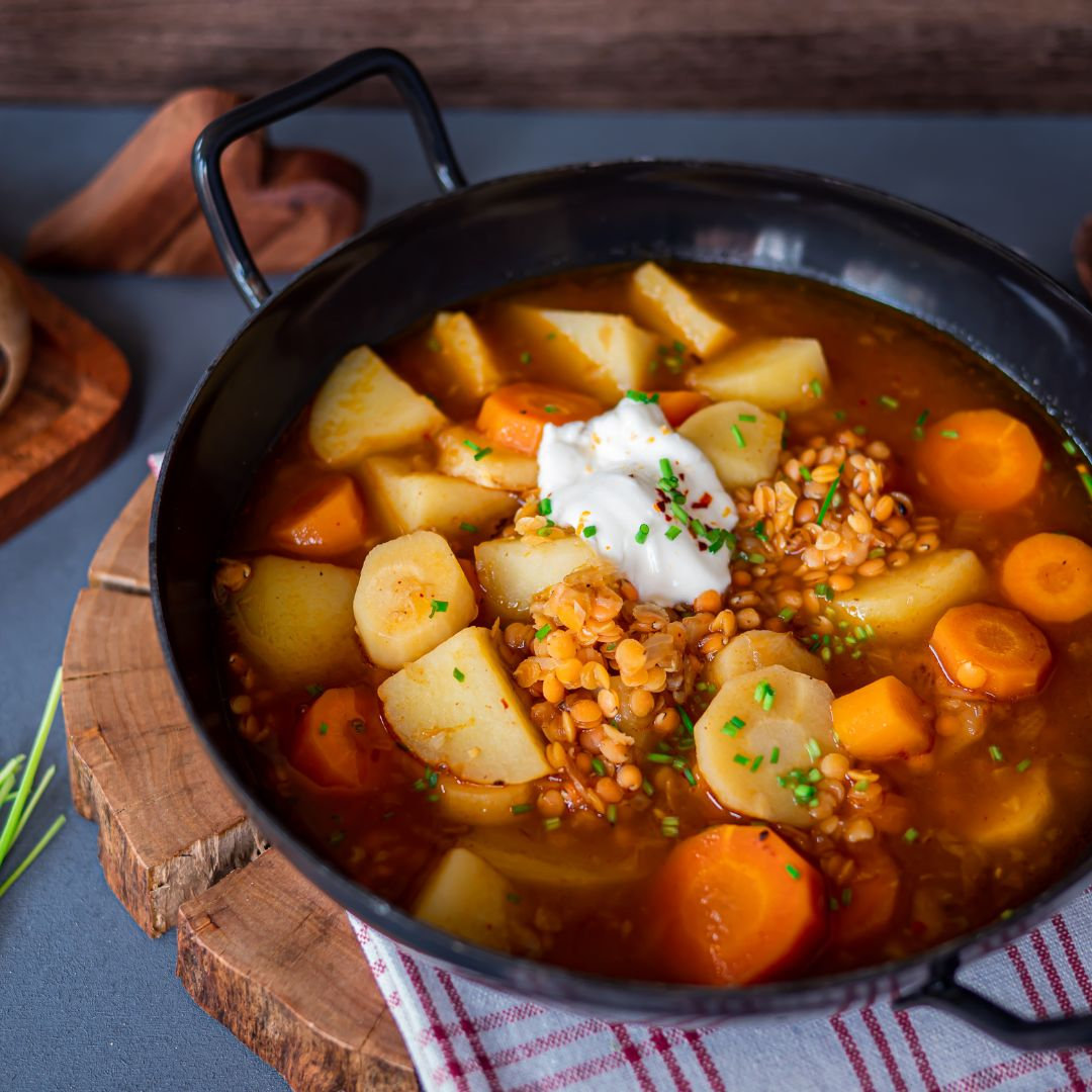 Eine Schale vegetarische Gulaschsuppe, garniert mit frischer Petersilie und einem Klecks Schmand, daneben Weißbrot.
