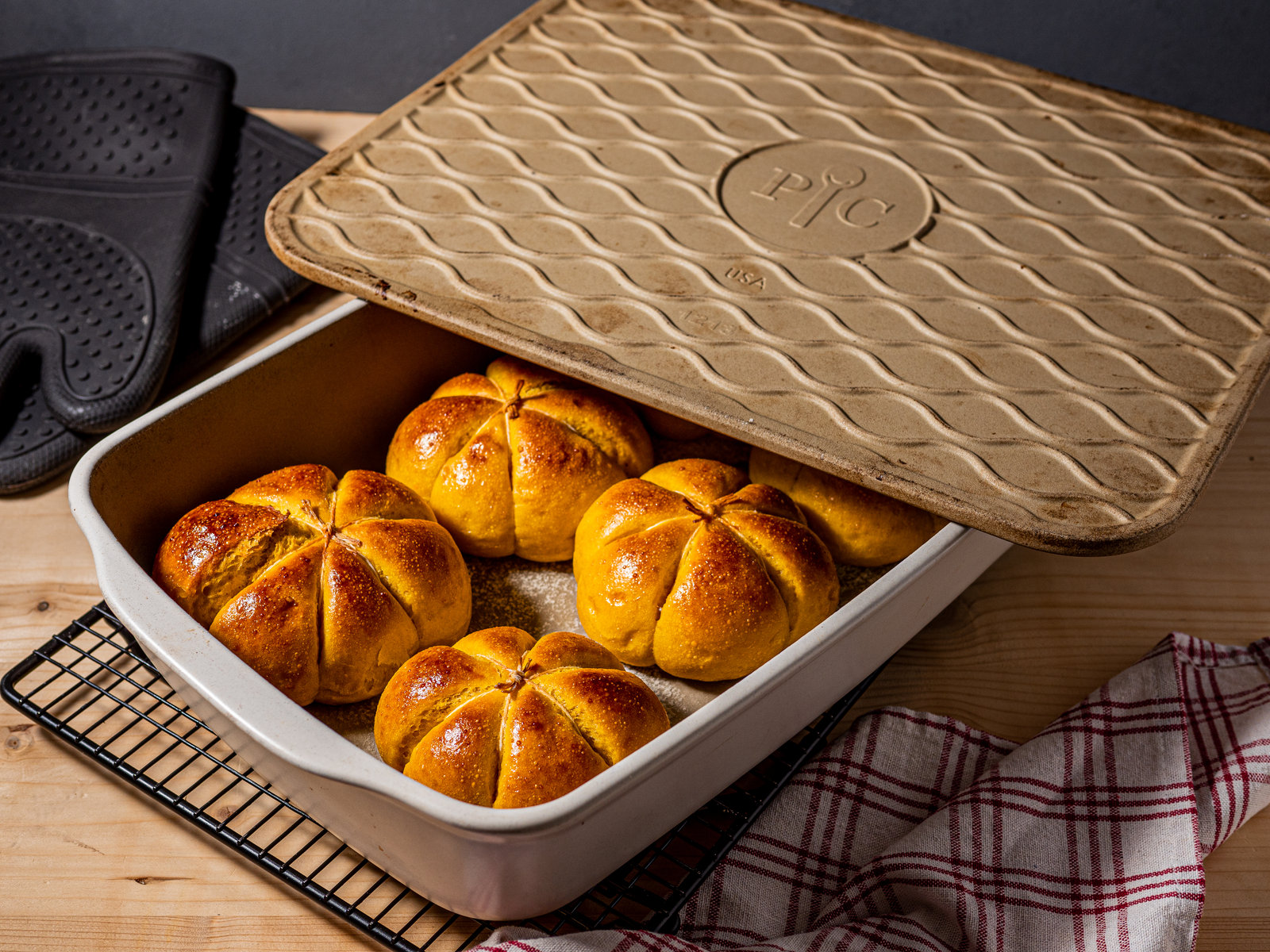 Sechs goldbraune Kürbis-Joghurt-Brötchen in Kürbisform auf einer Ofenhexe.