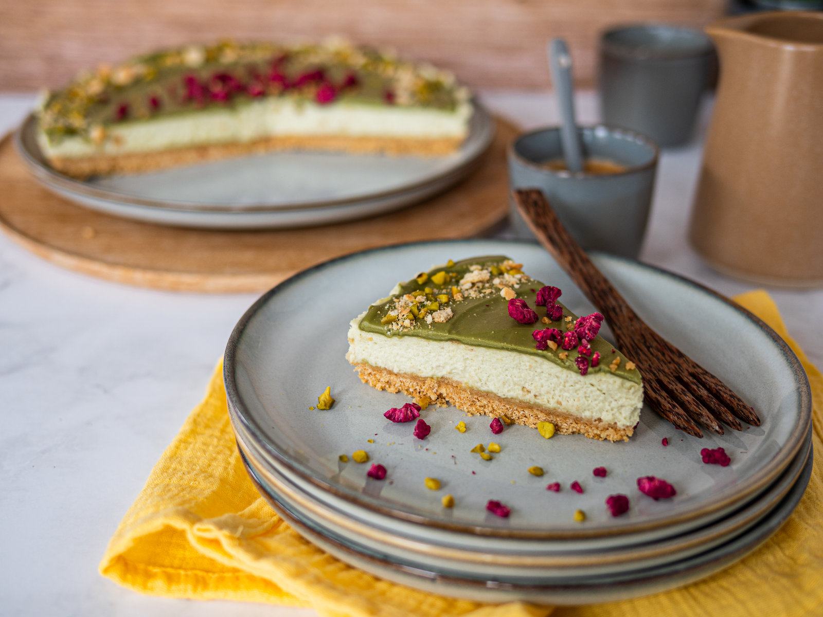 Eine angeschnittene No Bake Pistazien Tarte mit grünlicher Füllung, dekoriert mit gehackten Pistazien und Himbeeren.