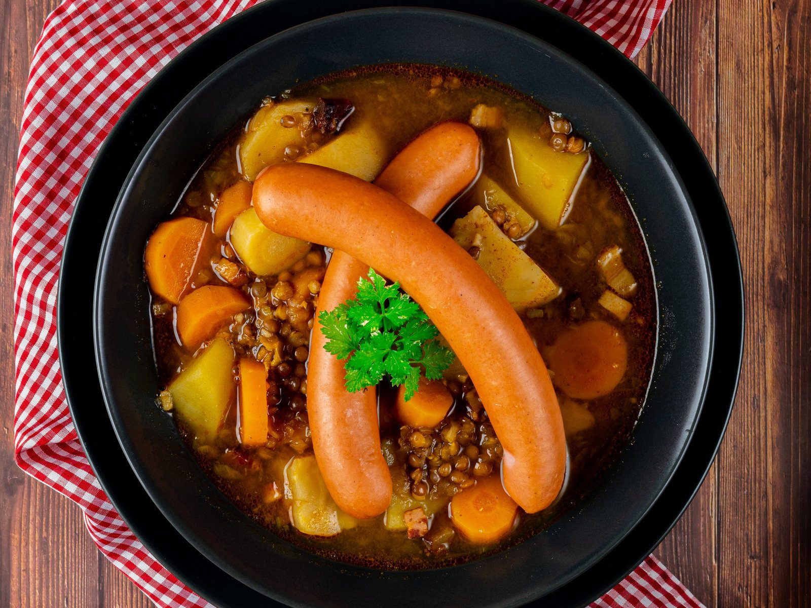 Deftige Berglinsensuppe mit Würsteln in einer Schüssel, garniert mit frischen Kräutern.