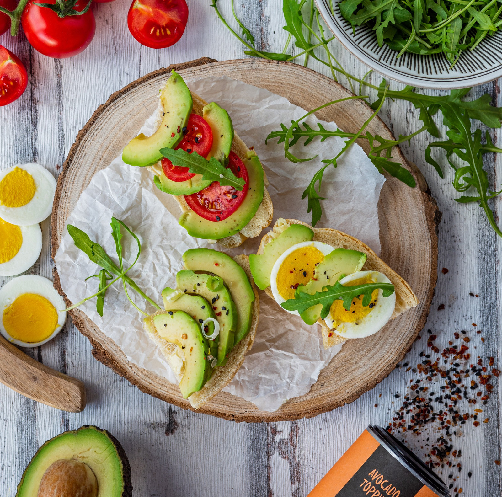 Zwei Scheiben Avocado Brot mit Tomaten, Eiern und Rucola auf einem Teller angerichtet.