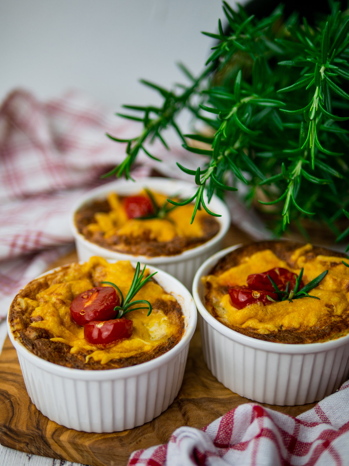 Zwei goldbraun gebackene Thunfisch Soufflés in kleinen Förmchen, mit geschmolzenem Käse überbacken.
