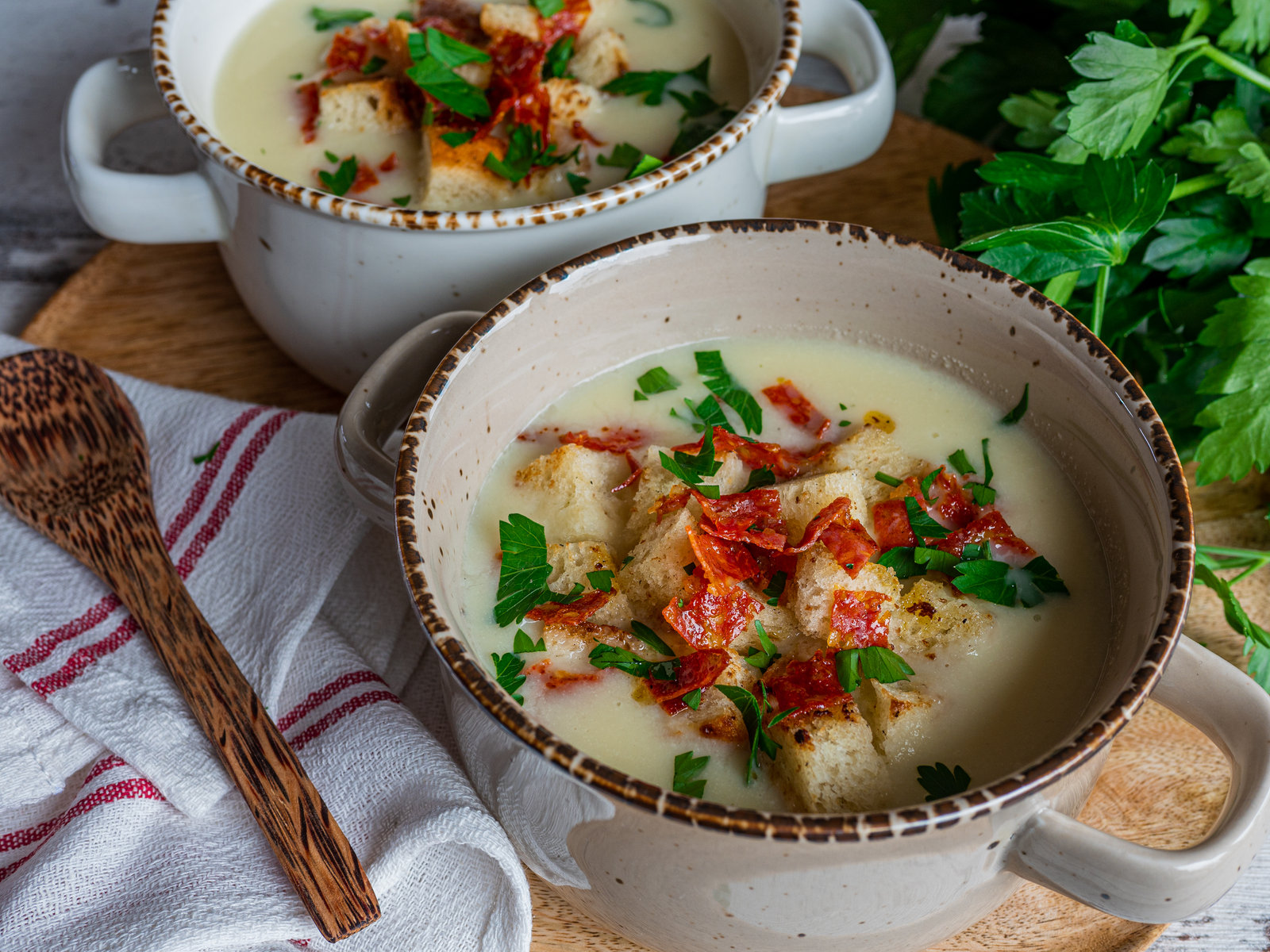 Eine Schale cremige Blumenkohlsuppe, garniert mit Wurstwürfeln, Brotcroutons und frischer Petersilie.