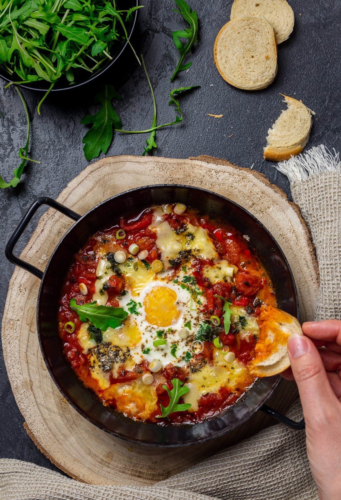 Shakshuka mit Camembert und Eiern in einer Pfanne, garniert mit frischen Kräutern