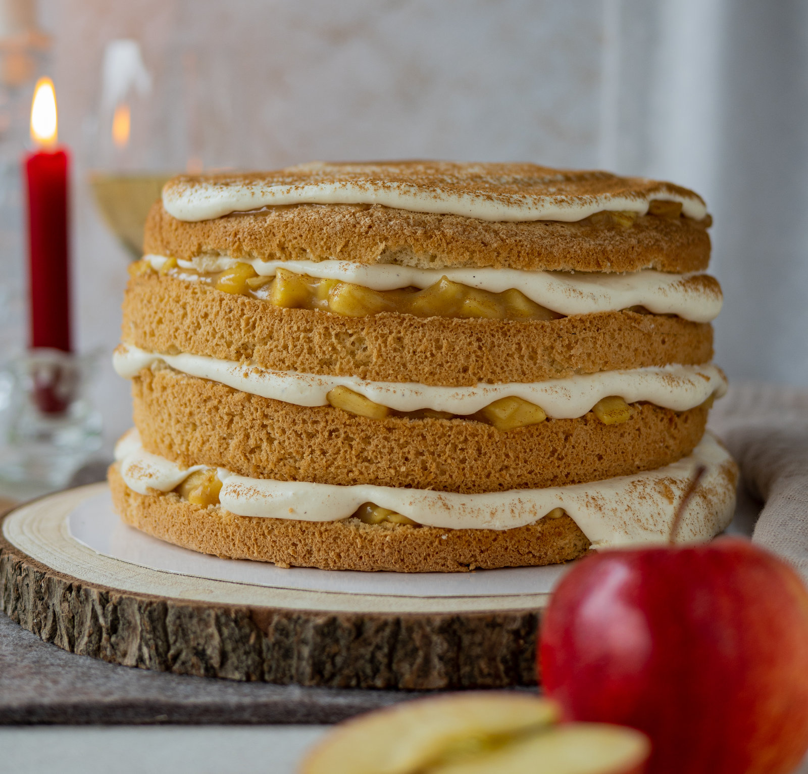 Anschnitt einer Apfel-Wein-Torte mit mehreren Schichten Biskuit, Apfelfüllung und heller Creme, bestreut mit Zimt.