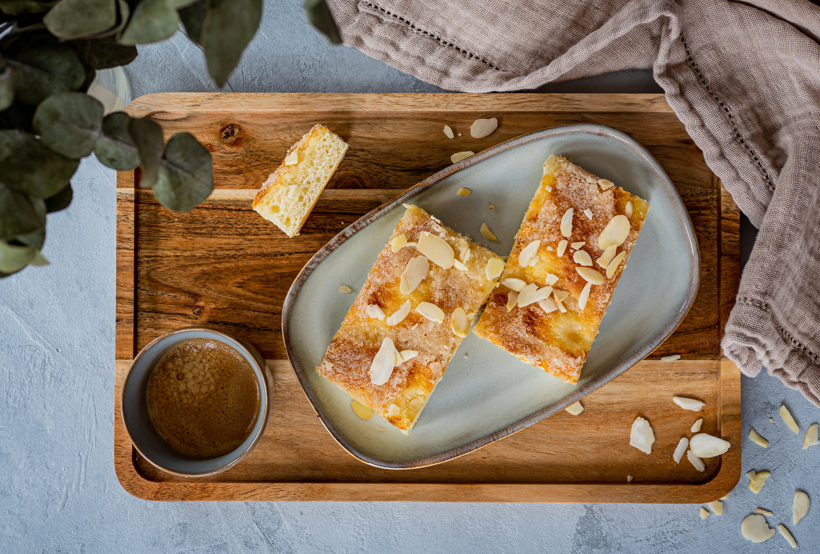Ein frisch gebackener Butterkuchen mit goldbrauner Kruste, Butterstücken und Mandelblättern auf einem Backblech.