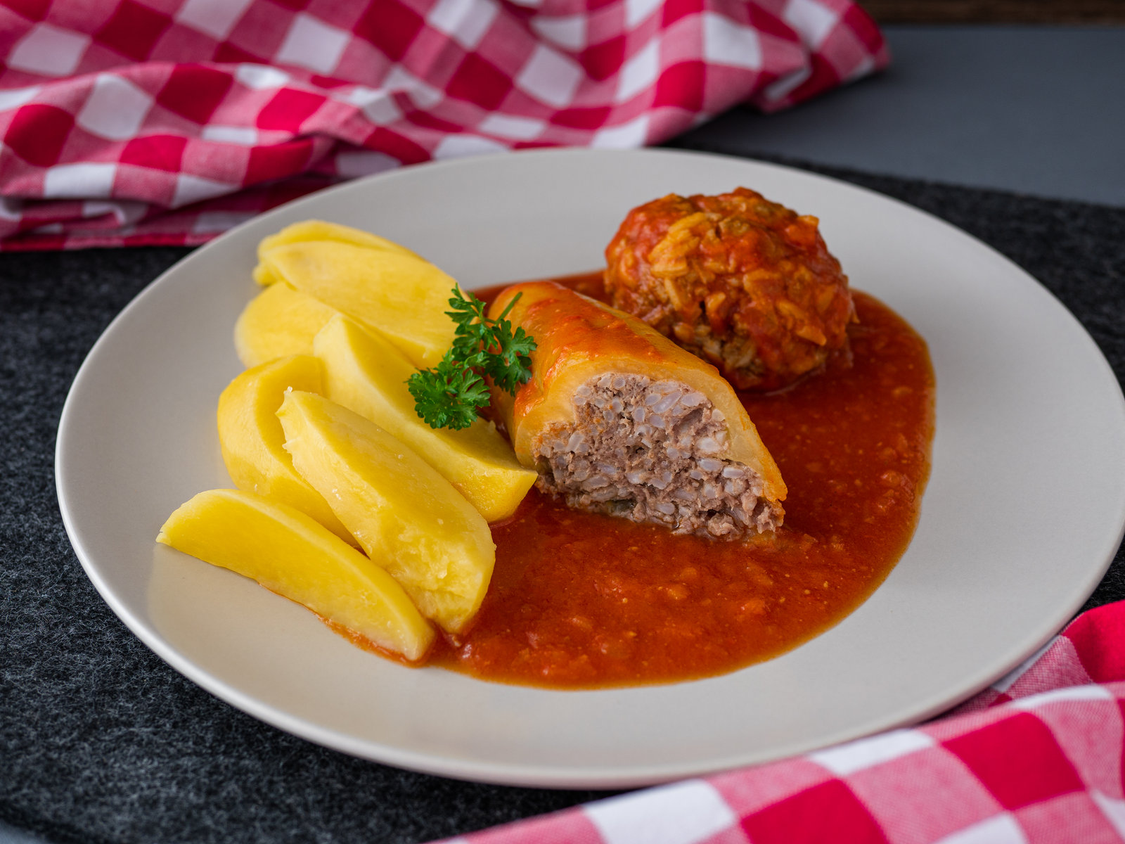 Gefüllte gelbe Paprika in Tomatensauce mit Kartoffelspalten auf einem Teller