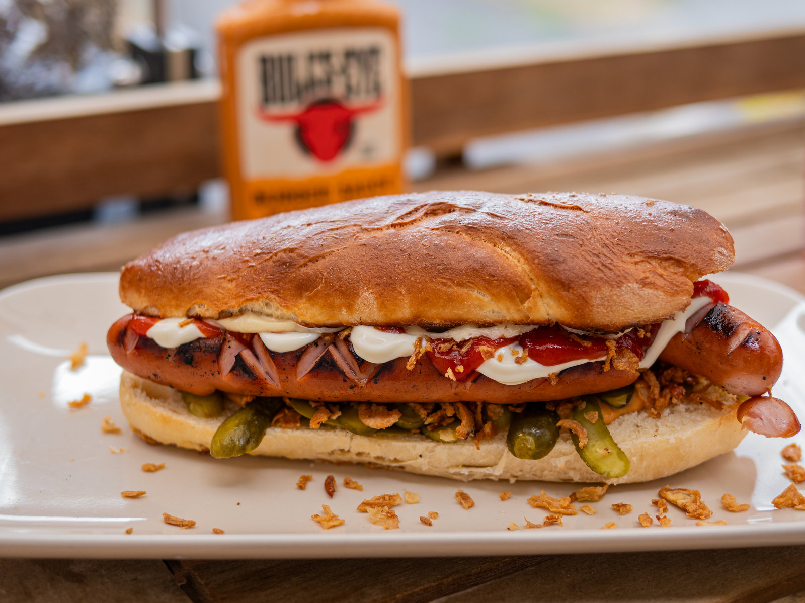 Ein Hot Dog mit selbstgebackenem Brötchen, Würstchen, Röstzwiebeln und Saucen