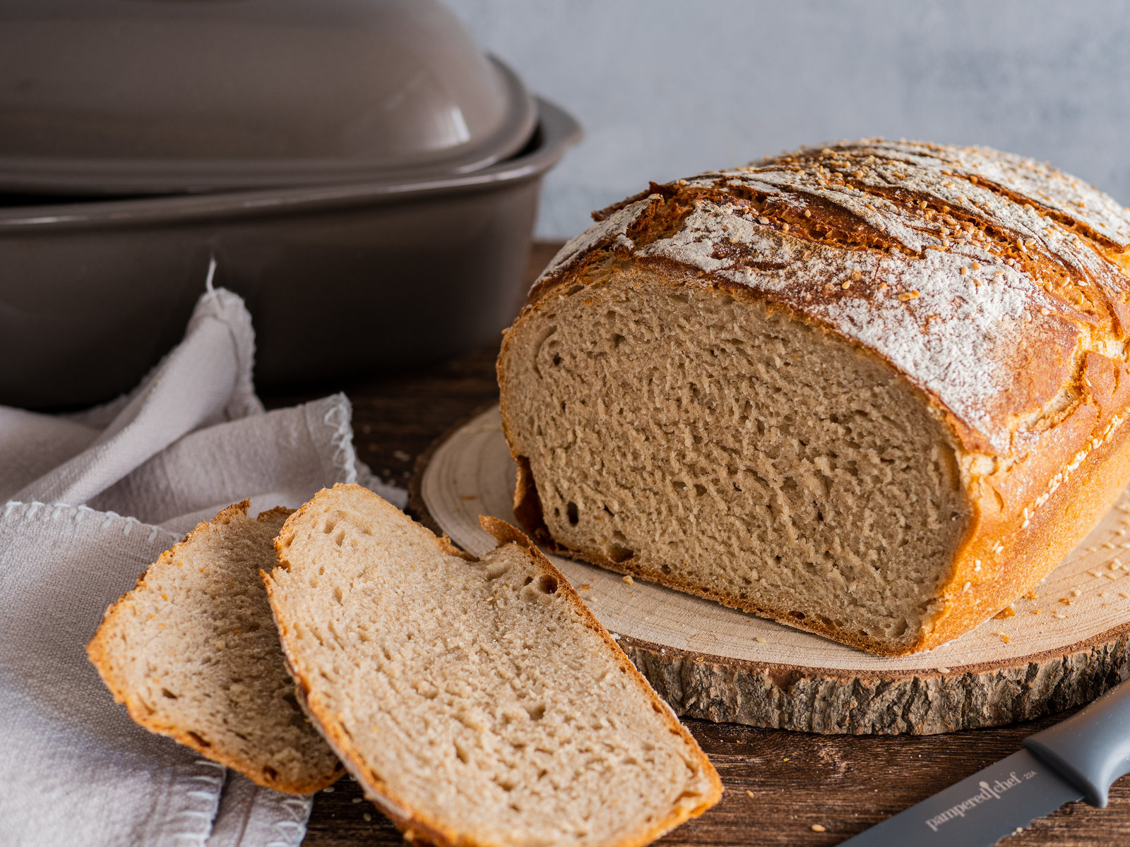 Ein frisch gebackenes, angeschnittenes Mischbrot mit Sesam auf einem Holzbrett.