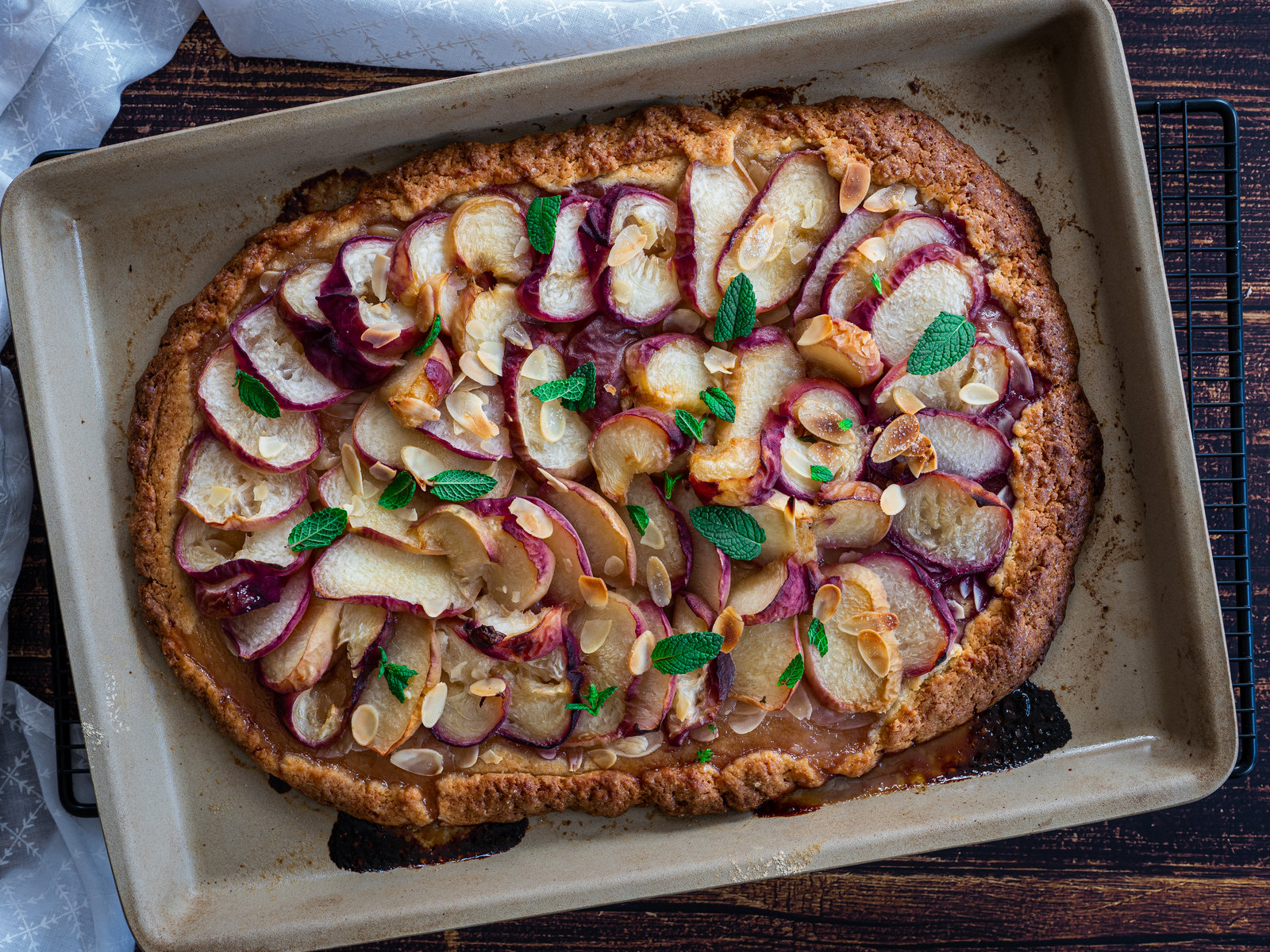 Eine frisch gebackene Pfirsich Galette, rustikal geformt und mit Puderzucker bestäubt, auf einem Backblech.
