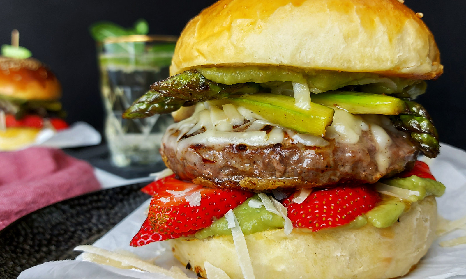 Ein Wildburger mit Avocado, Spargel und Erdbeeren auf einem Teller angerichtet.