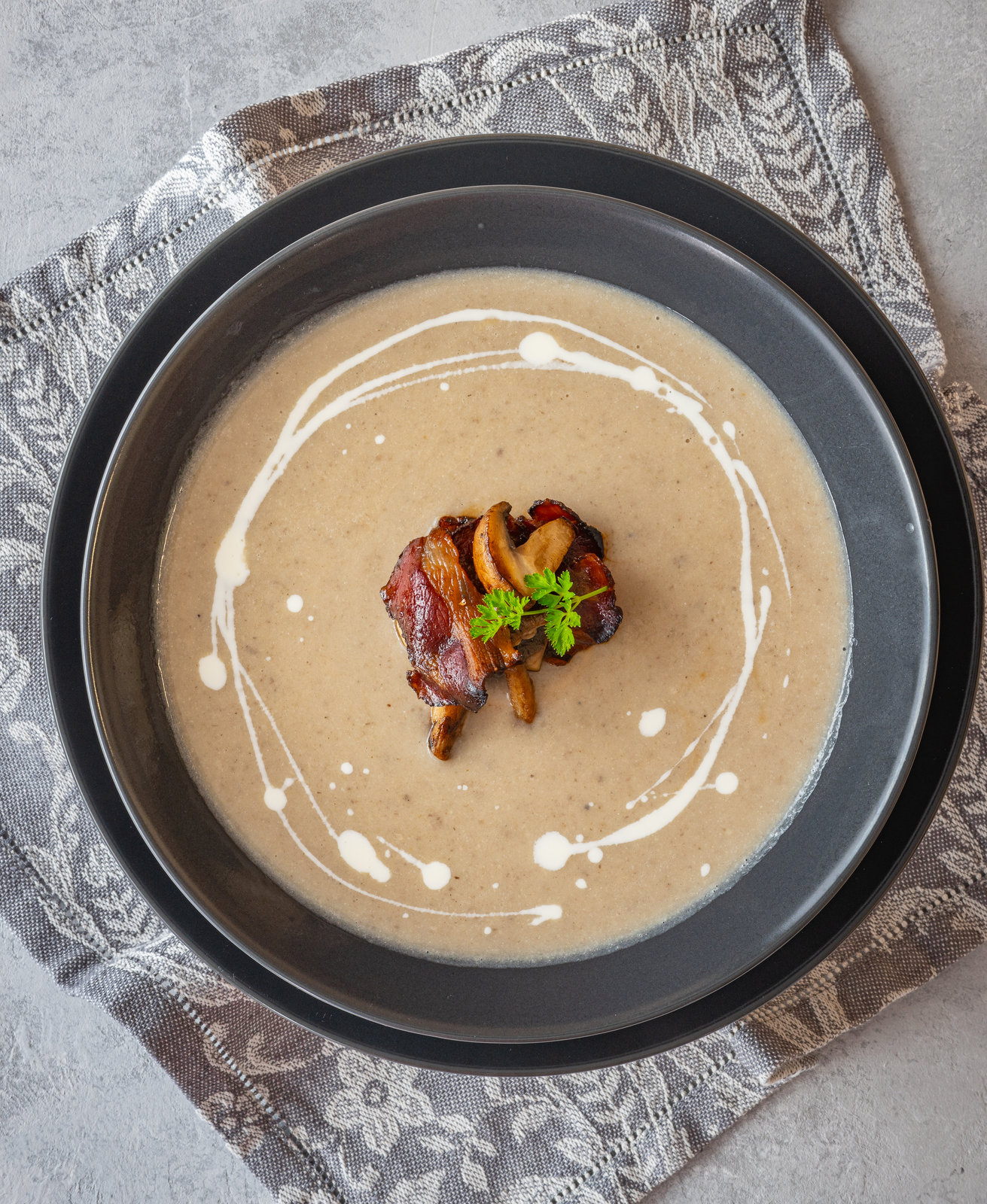 Eine Schale cremige Champignon-Suppe, garniert mit gebratenen Champignons und knusprigem Speck.