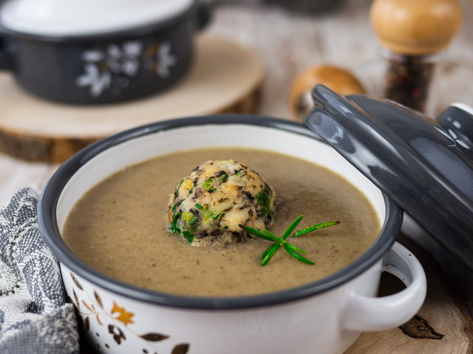 Cremige Champignon-Suppe in einer Schale, garniert mit frischen Kräutern und Semmelknödeln.